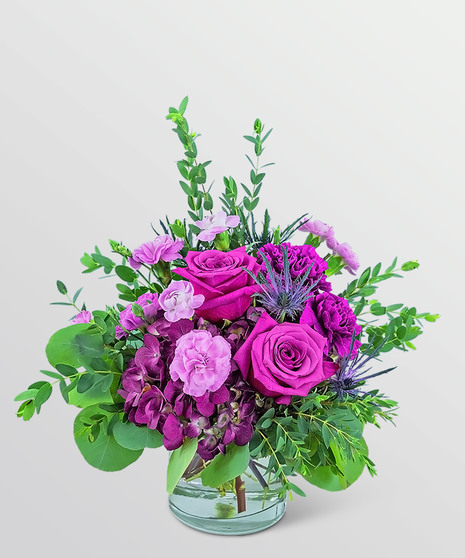 magenta flowers with green filler around them in a low glass container